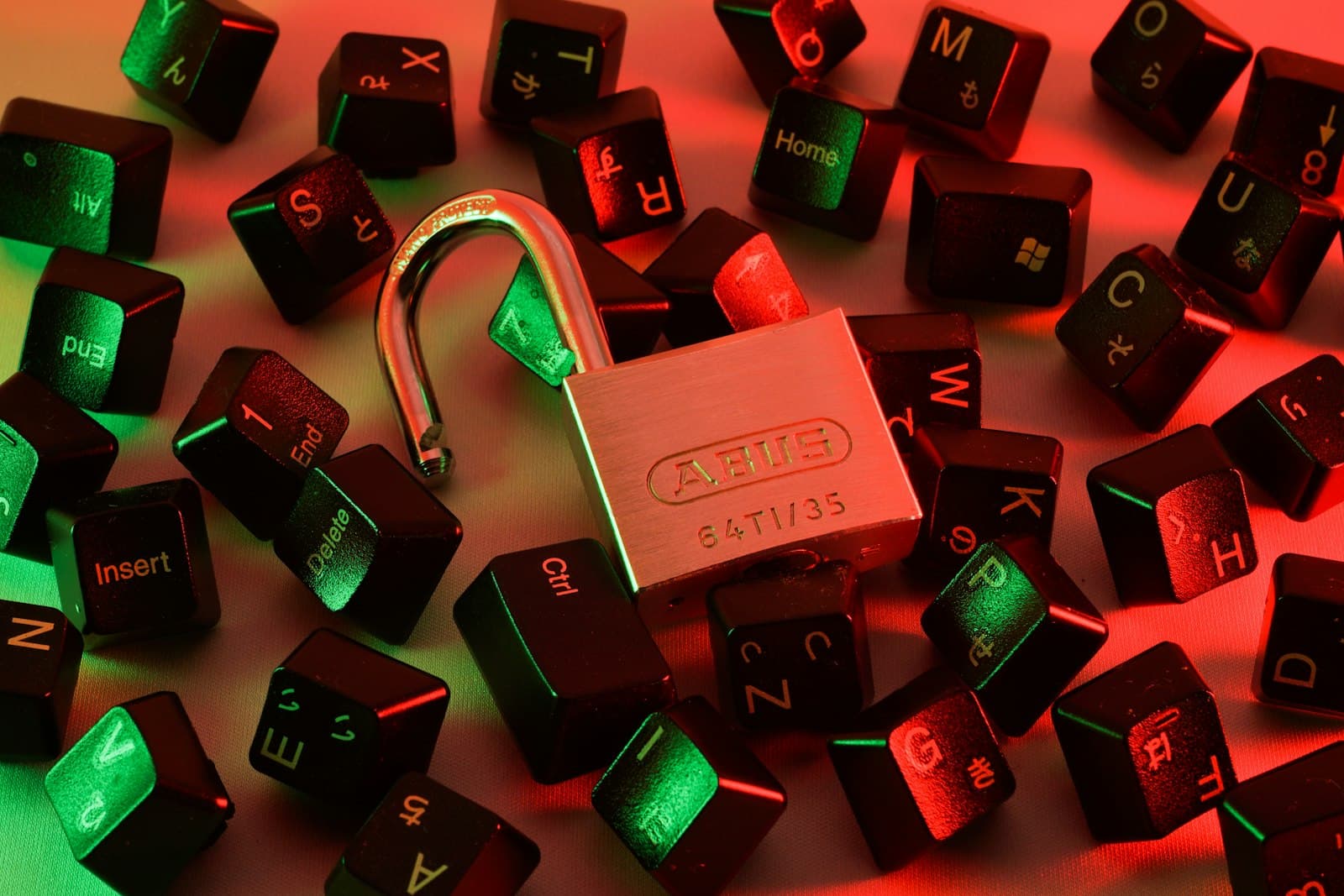 An open padlock among scattered keyboard keys under red and green light, photo by FlyD / Unsplash